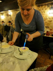 Katalanische Creme die im Restaurant von einer Dame am Tisch karamellisiert wird